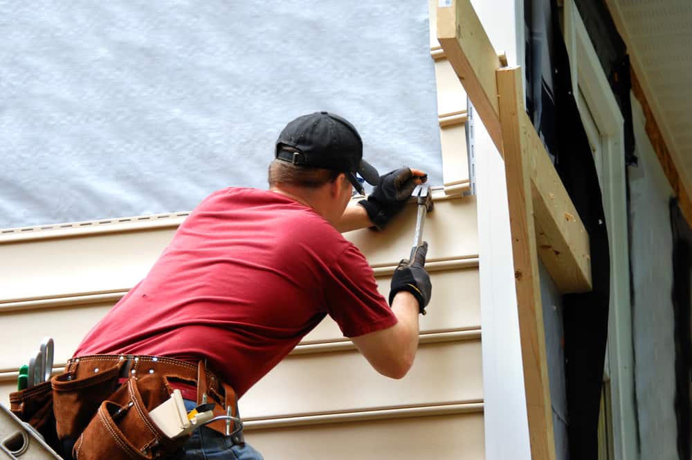 Young Homeowner Installs Siding To A Home. He Is Holding A Hammer